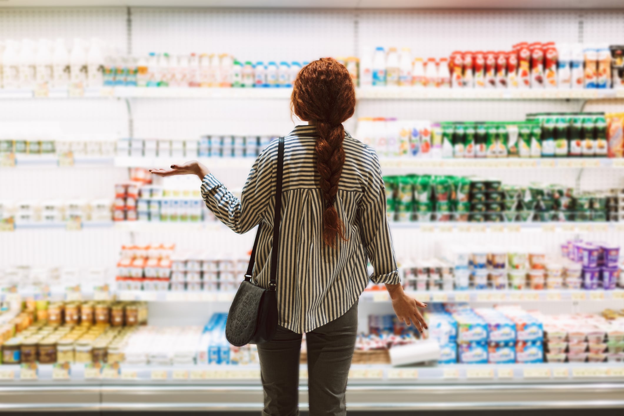 Young woman in striped shirt from back trying choose dairy products in modern supermarket